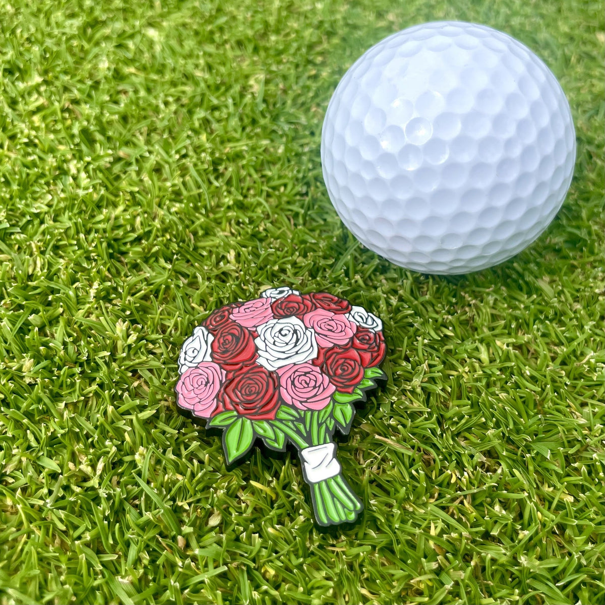 Ballmarker Rosen von Alpha Putts neben einem Golfball auf dem Grün